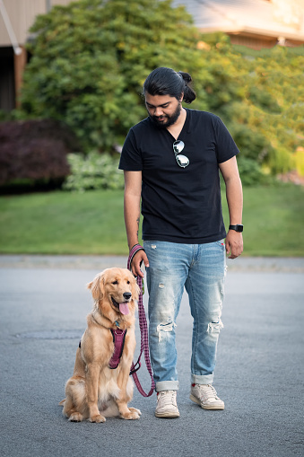 Patient Hispanic young man walking his young golden retriever dog on a leash.  North Vancouver, British Columbia, Canada.
