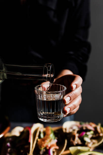 メキシコの背景にタコスと食べ物と伝統的なガラスでメキシコのメスカルショットを提供するバーマンの手 - drink mexican culture tequila shot tequila ストックフォトと画像