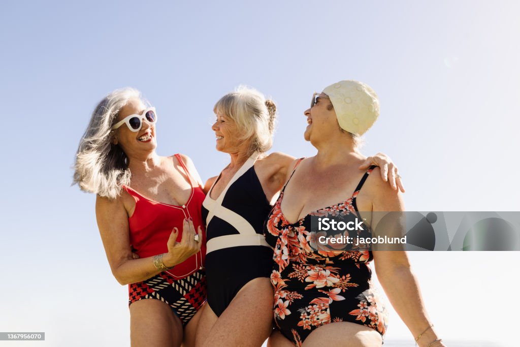 Group of happy elderly women having fun in swimwear Group of cheerful elderly women having fun during summer vacation. Happy senior women laughing and embracing each other while wearing swimsuits. Mature women enjoying themselves after retirement. Senior Adult Stock Photo