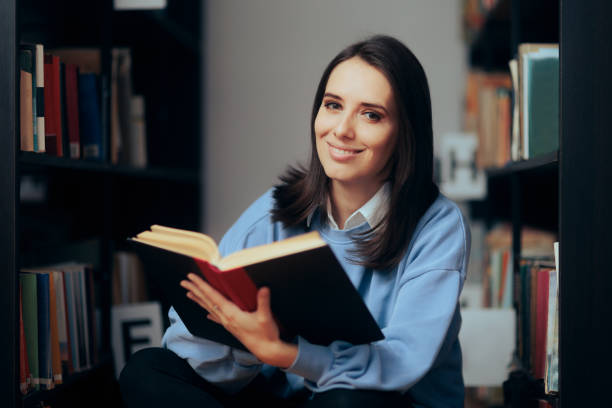 istock Happy Cheerful Woman Reading a Book in the Library 1367957734