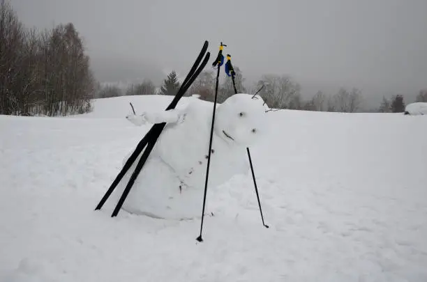 Photo of The big snowman has a tilted body that looks like he's falling. has ski poles and cross-country skis. jumping mascot. slow melting and freezing tilts the center of gravity