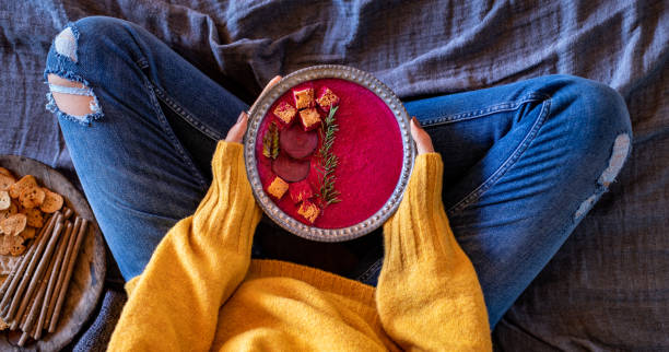 A young girl lye on her bed and drinking her beetroot soup.