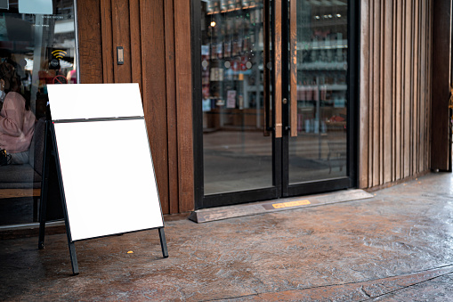 The white blank sheet is placed on located in front of a coffee shop. Blank wood sandwich board standing outdoor cafe, mockup menu advertising design.
