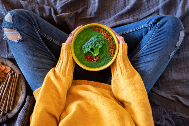 A young girl lye on her bed and drinking her broccoli and spinach soup.