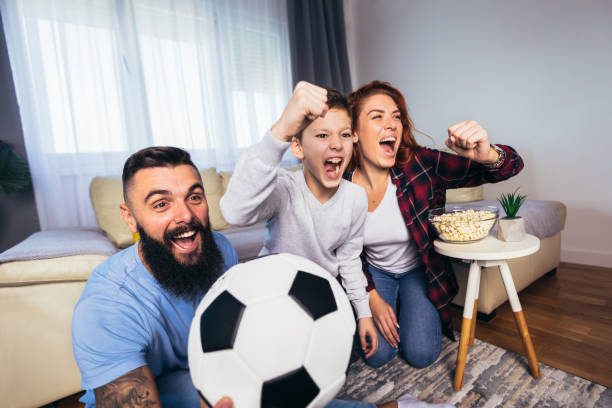 Family of fans watching a football match on TV at home stock photo