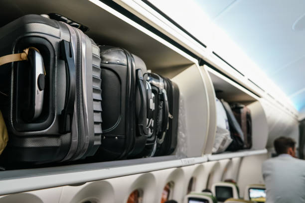 Airplane overhead locker with black plastic baggage suitcases, closeup detail stock photo
