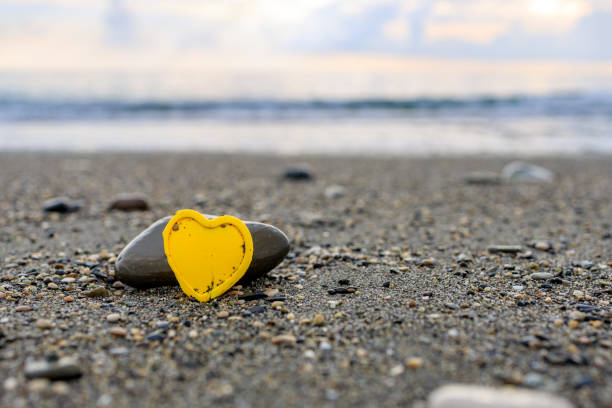 yellow plastic heart on the seashore, stone and heart. love for the sea