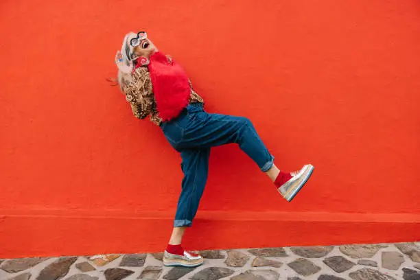 Photo of Excited senior woman dancing and having fun against a red wall