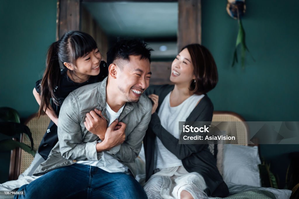 Playful young Asian family having fun playing at home while mother and daughter tickling father in bed. Family life with love and happiness Family Stock Photo