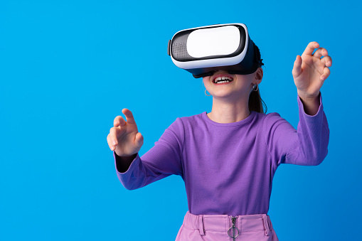 Girl with virtual reality glasses on blue background, close up