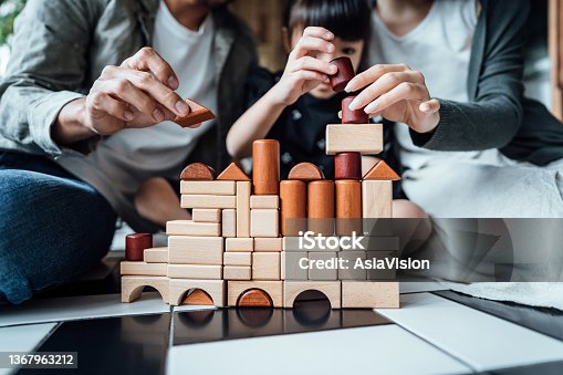 istock Close up of joyful young Asian family sitting on the floor in the living room having fun playing wooden building blocks with daughter together at home 1367963212