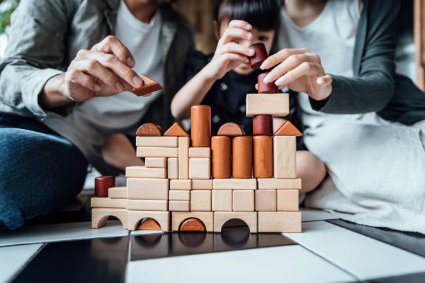 Close up of joyful young Asian family sitting on the floor in the living room having fun playing wooden building blocks with daughter together at home stock photo