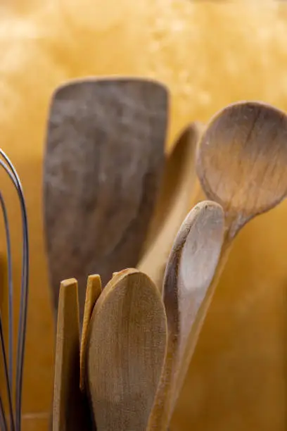 Set of old rustic wooden kitchen utensils and salad servers with selective focus to the spoon and fork over an ochre yellow background