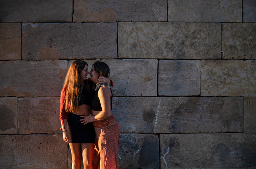 Two girls who are couple standing against stone wall during sunset. Madrid, Spain