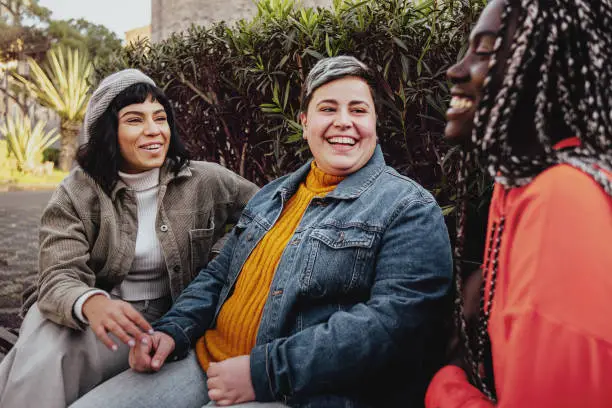 Interracial cheerful group of happy girls having fun talking together in the park talking and having fun sitting on a bench in the park