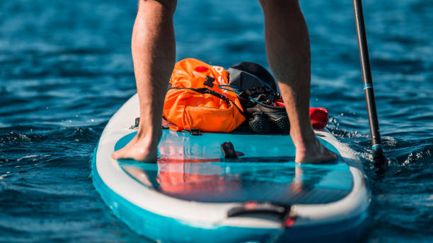 Young athletic man paddling on a SUP stand up paddle board in blue water sea in Montenegro Young athletic man paddling on a SUP stand up paddle board in blue water sea in Montenegro paddleboard photos stock pictures, royalty-free photos & images
