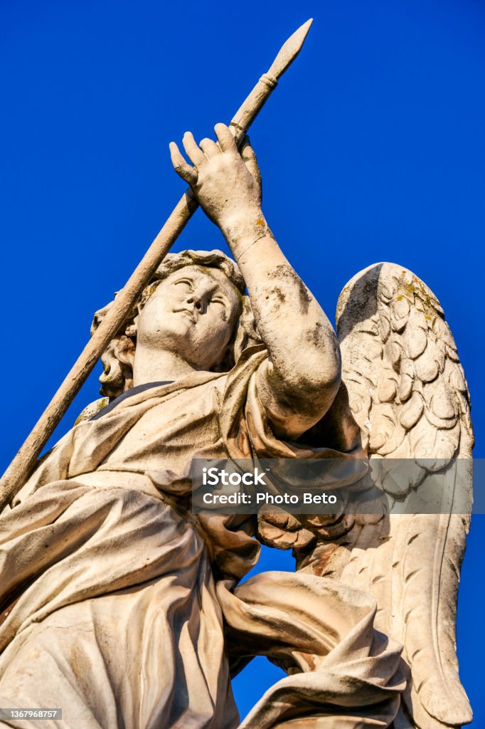 The detail of a statue of an Angel by Bernini in the historic and baroque heart of Rome The detail of one of the monumental statues of angels along the Ponte Sant'Angelo (Saint Angel bridge), in the historic and baroque heart of Rome. This bridge was built under the emperor Hadrian in 134 AD. to connect the heart of Rome with his mausoleum, currently Castel Sant'Angelo. A few centuries later, under the pontificate of Pope Clement IX, the architect and sculptor Giovanni Lorenzo Bernini was commissioned to create the current balustrade decorated with ten statues of the Angels of the Passion of Christ. According to the Christian tradition, each Angel holds one of the relics of the Passion of Christ, such as the cross, the veil of Veronica, the nails, the spear, the pillar of the scourging, etc. Designed by Bernini, the statues were made under his direction in 1669 by the pupils present in his school of sculpture. In 1980 the historic center of Rome was declared a World Heritage Site by Unesco. Image in high definition image. Rome - Italy Stock Photo
