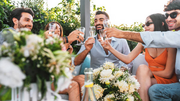 amigos que se reúnen en la terraza y brindan con champán sentados en el sofá: los mejores amigos se divierten bebiendo vino espumoso en el jardín de lujo - croquet party front or back yard wedding fotografías e imágenes de stock