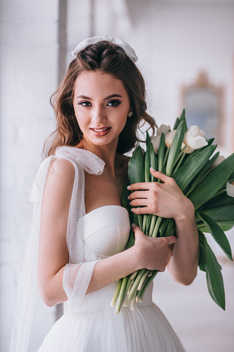 Happy beautiful bride holding wedding bouquet of white tulips in her hands in studio. Wedding day