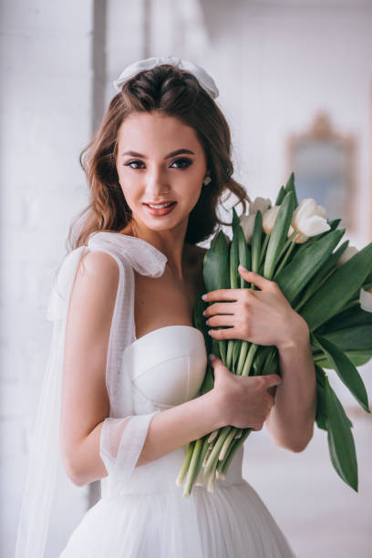 Happy beautiful bride holding wedding bouquet of white tulips in her hands in studio. stock photo