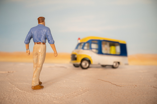 A man approaches an ice cream van in the desert. Scale model photography.
