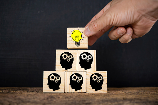 Man holding a cube with a lightbulb symbol placed on a cog-headed businessman. Teamwork building your ideas is an easy way to solve problems.