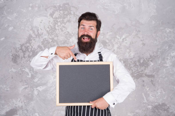 istock Man good looking hipster cafe barista with blackboard copy space, restaurant menu concept 1367978137