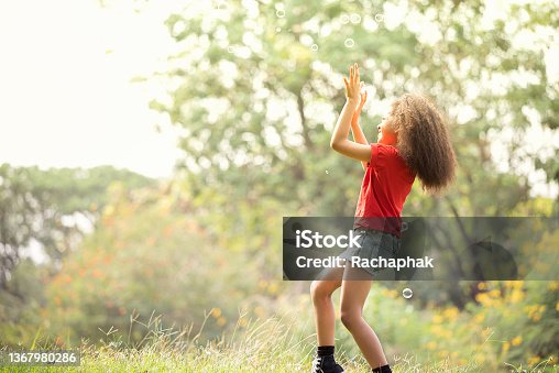 istock African-American girl enjoying playing with soap bubbles in autumn park. 1367980286