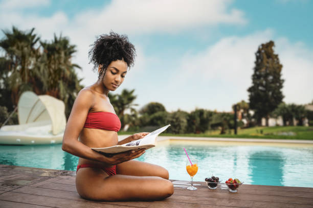 афроамериканка читает журнал и завтракает фруктами у бассейна - swimwear bikini swimming pool red стоковые фото и изображения