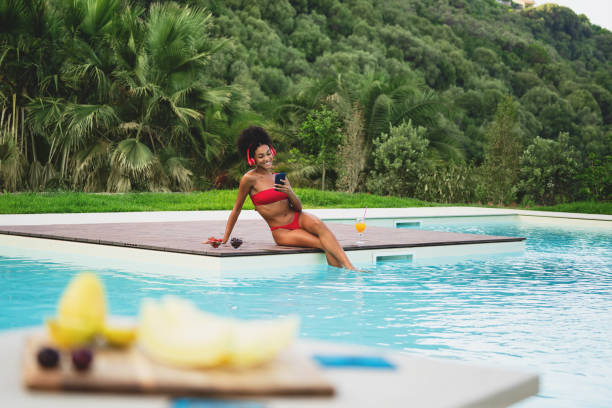 mujer afroamericana escuchando música junto a la piscina - swimwear bikini swimming pool red fotografías e imágenes de stock