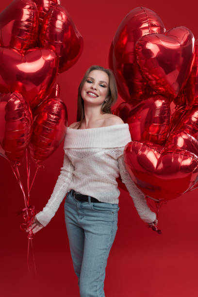 Young woman with bunch of balloons having fun on red background. stock photo