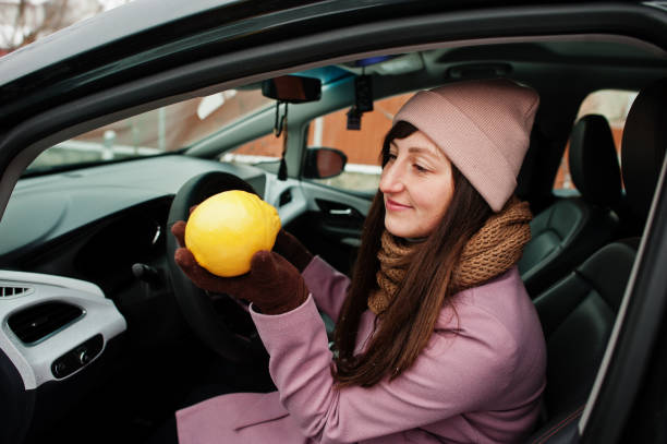 istock Young woman sit in car and sniffs a lemon at winter. 1367982339