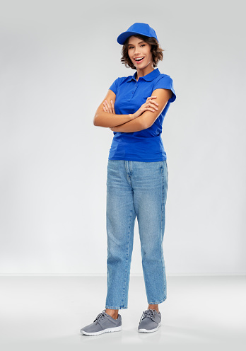 service and people concept - happy smiling delivery woman in blue uniform with crossed arms over grey background
