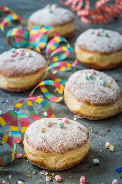 istock Krapfen, Berliner or donuts with streamers, confetti and mini marshmallows on gray background. Colorful carnival or birthday image, vertical 1367985082