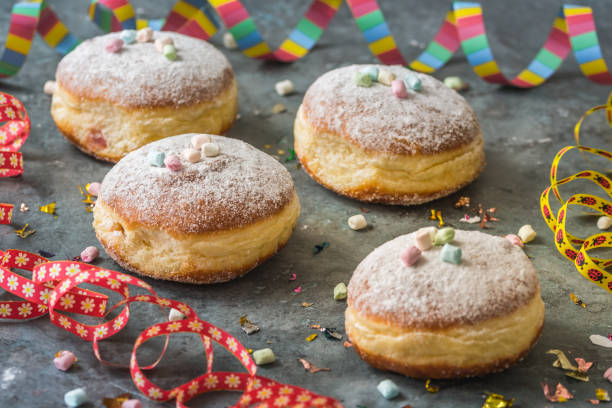 istock Krapfen, Berliner or donuts with streamers, confetti and mini marshmallows on gray background. Colorful carnival or birthday image 1367985090