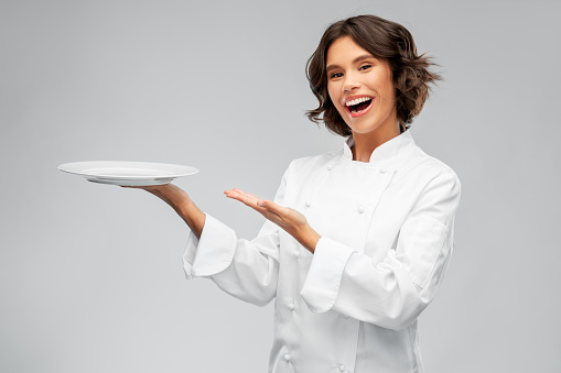 cooking, advertisement and people concept - happy smiling female chef holding empty plate over grey background