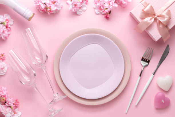 istock Place setting for Valentine's Day. Romantic dinner, table setting with cutlery. Pink background. Dating concept, love. Spring flowers, empty plate, glasses, champagne, holiday gift box. 1367985249