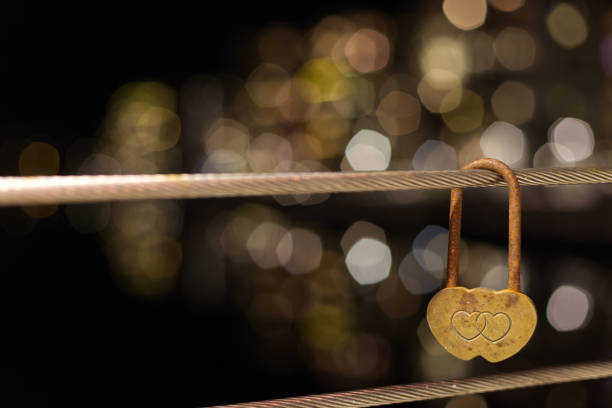 Night image of a heart shaped lock on a bridge with some nice blurred lights behind it. Good image for valentines day and to talk about love. Warm colours. Plenty copy space.