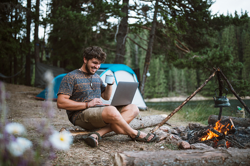 Smiling young man next to the campfire using technology.