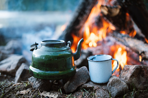 Close up of vintage teapot and cup next to campfire.