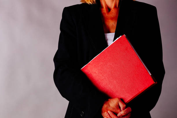 Mature business woman holding a folder in front of a plain background.