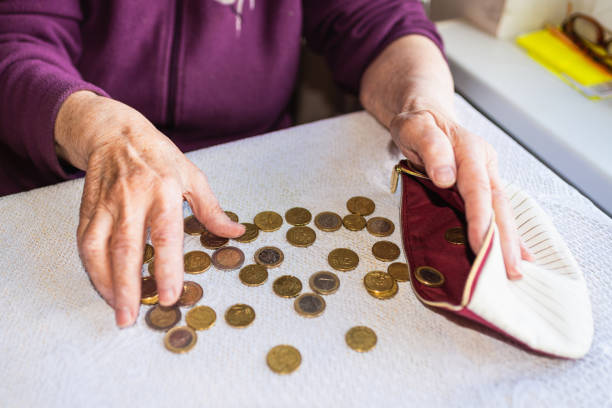 vecchia donna seduta miseramente a casa e contando le monete rimanenti della pensione nel suo portafoglio dopo aver pagato le bollette. - miseramente foto e immagini stock