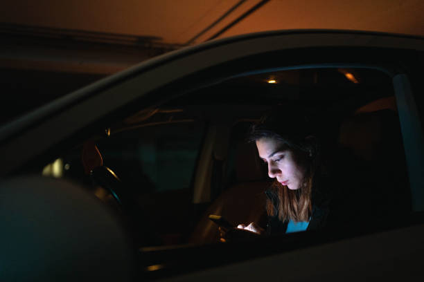 adolescente caucasiana, sentada no carro e usando celular - teenager dark pensive emotional stress - fotografias e filmes do acervo