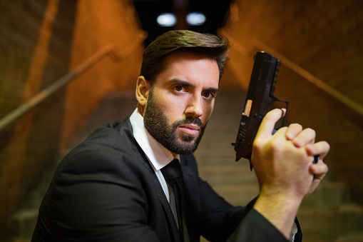 Portrait of serious and confident Caucasian man in suit, in a role of bodyguard or secret agent, holding the pistol