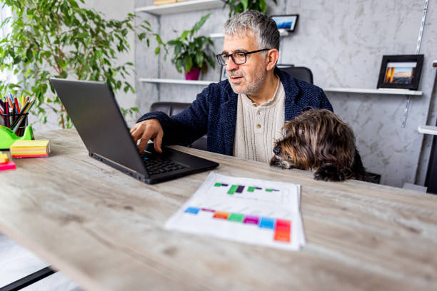 istock Mature man working on laptop in home office while his dog looking 1367994037