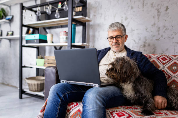 istock Man using laptop on sofa, his pet dog lying next to him 1367994250