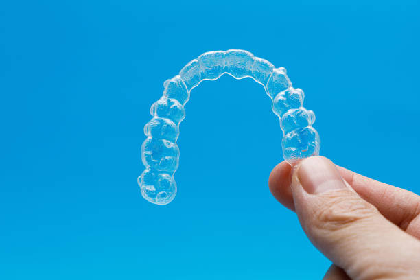 istock Hand holding one transparent retainer on blue background. Invisalign orthodontics concept 1367995485