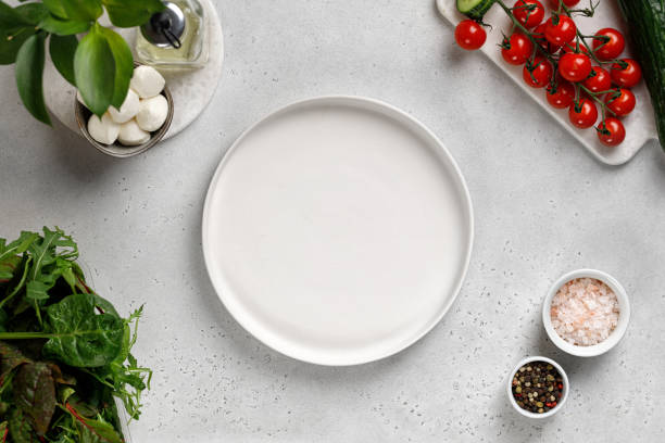istock White empty plate for salad. Ingredients for salad cucumber slice, cherry tomatoes, mozzarella, mix salad. Top view. 1367996496