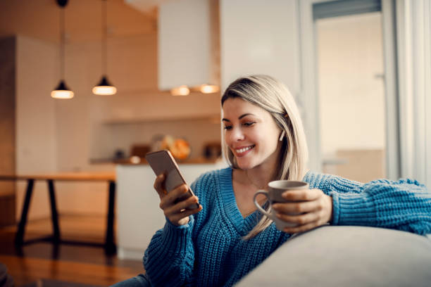 una mujer feliz colgada en las redes sociales por teléfono y tomando café en su casa. - hot drink audio fotografías e imágenes de stock