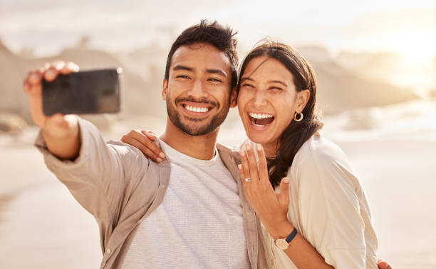 scatto di una giovane coppia che scatta selfie in spiaggia - engagement foto e immagini stock